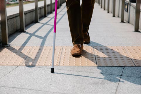 Persona caminando con bastón blanco sobre piso podotáctil